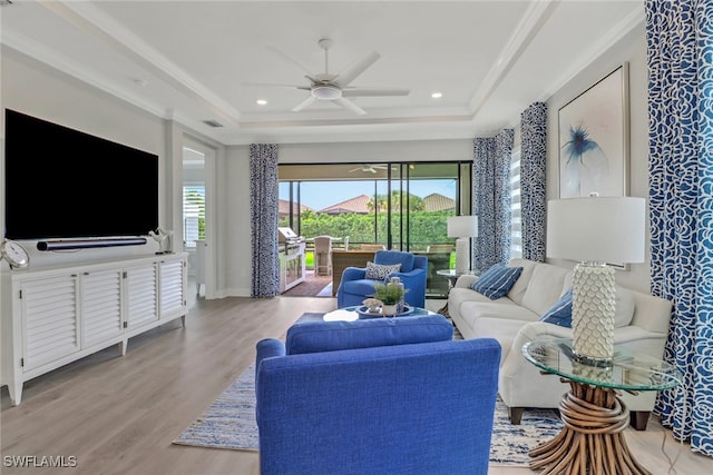 living area with light wood finished floors, ornamental molding, a raised ceiling, and a ceiling fan