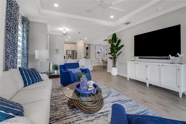 living room with crown molding, a raised ceiling, a ceiling fan, and light wood-style floors