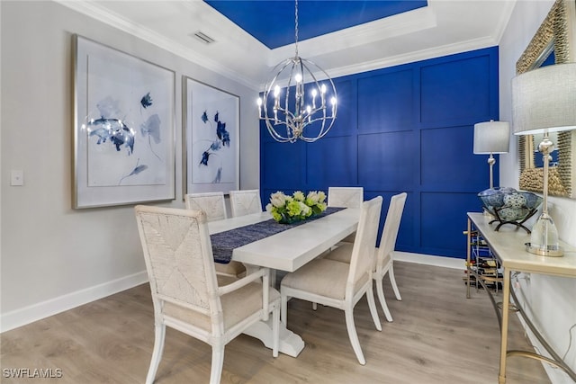 dining area with an inviting chandelier, visible vents, a decorative wall, and a tray ceiling