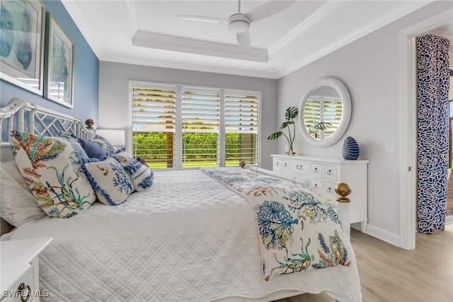 bedroom with light wood finished floors, ceiling fan, a tray ceiling, and ornamental molding