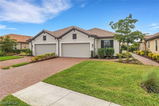 mediterranean / spanish home featuring a garage, a tiled roof, decorative driveway, stucco siding, and a front lawn