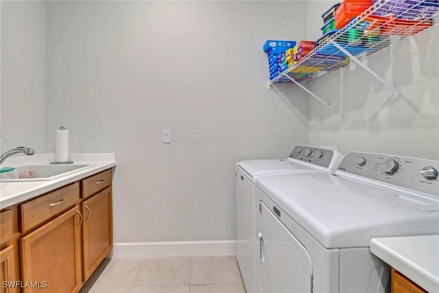 clothes washing area with cabinet space, light tile patterned flooring, a sink, washer and dryer, and baseboards