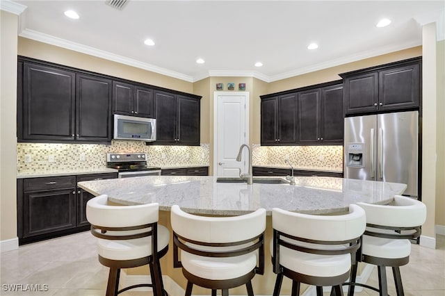 kitchen with a sink, light stone countertops, a kitchen bar, appliances with stainless steel finishes, and a kitchen island with sink