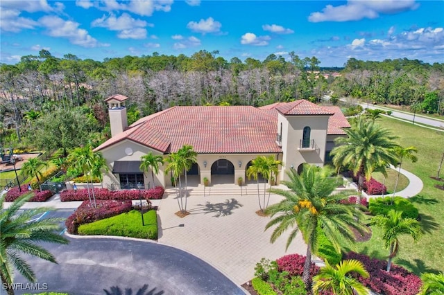 mediterranean / spanish home featuring a tile roof, driveway, a chimney, and stucco siding