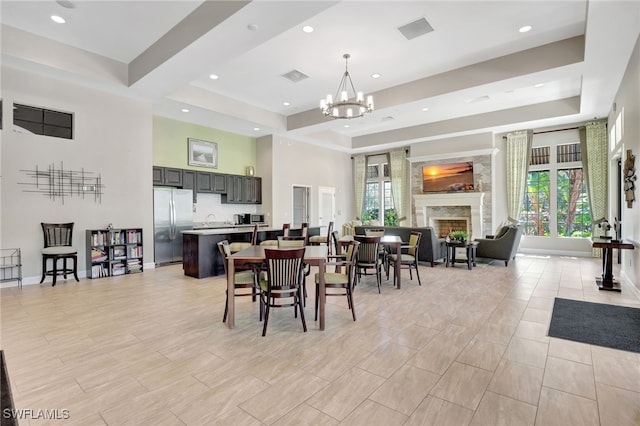 dining space with an inviting chandelier, a premium fireplace, visible vents, and a raised ceiling