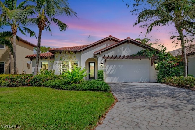 mediterranean / spanish home with decorative driveway, a tile roof, stucco siding, a lawn, and an attached garage