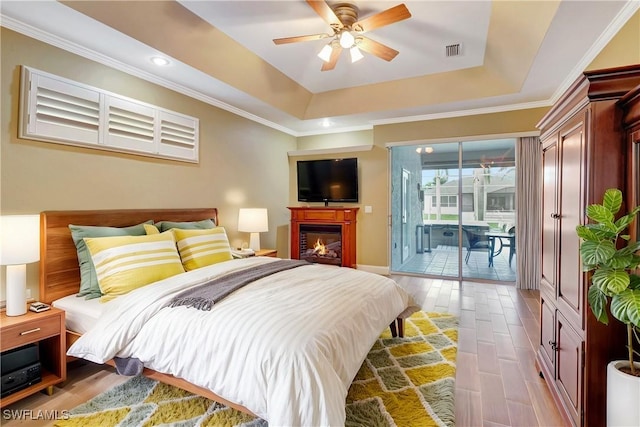 bedroom with wood finished floors, visible vents, access to outside, ornamental molding, and a tray ceiling