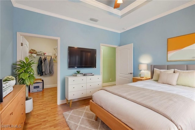 bedroom with light wood finished floors, baseboards, visible vents, a walk in closet, and crown molding