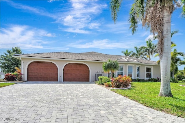 single story home with central air condition unit, a garage, decorative driveway, stucco siding, and a front yard