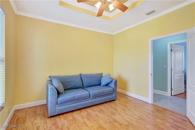 living area featuring baseboards, visible vents, a raised ceiling, ornamental molding, and wood finished floors