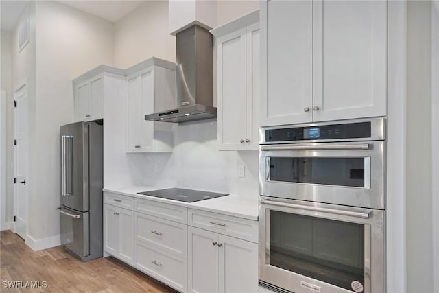 kitchen featuring wall chimney range hood, white cabinetry, stainless steel appliances, and light countertops