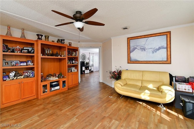 living room featuring light wood-style floors, visible vents, a textured ceiling, and ornamental molding