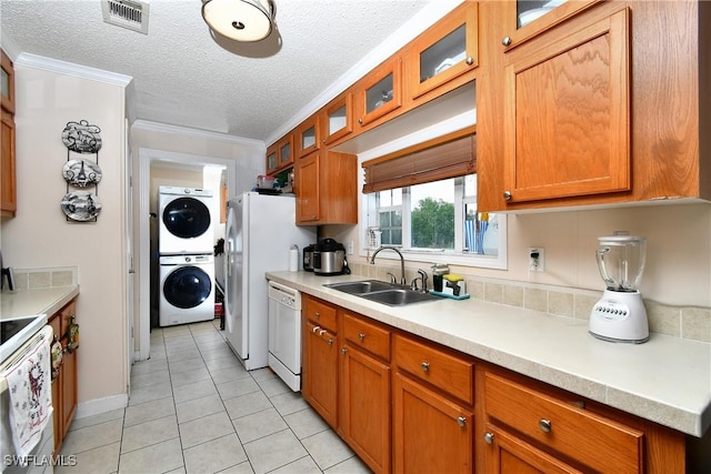 kitchen with white appliances, visible vents, brown cabinetry, stacked washer / drying machine, and a sink