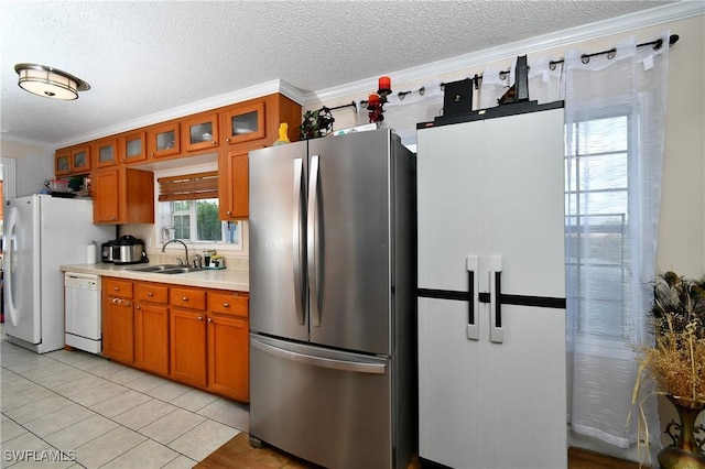 kitchen featuring white appliances, brown cabinetry, light countertops, crown molding, and a sink