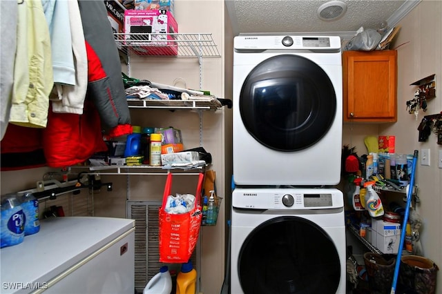 clothes washing area with a textured ceiling, stacked washer / dryer, and cabinet space