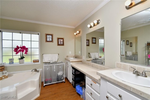 full bath featuring ornamental molding, wood finished floors, a garden tub, a textured ceiling, and vanity