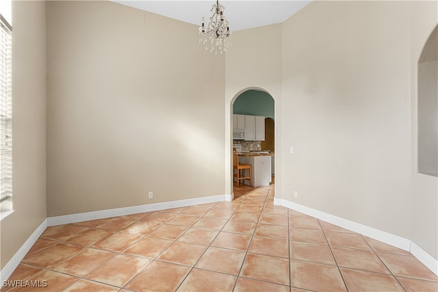 tiled spare room with a notable chandelier and a towering ceiling