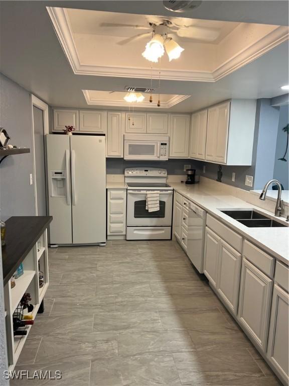 kitchen with white appliances, white cabinets, ceiling fan, a tray ceiling, and sink