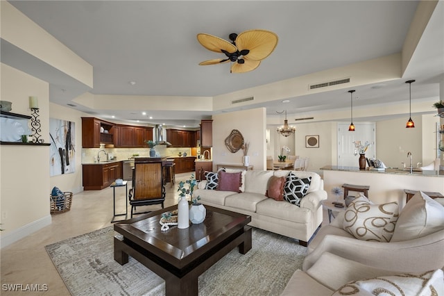 living room featuring ceiling fan with notable chandelier, a tray ceiling, visible vents, and baseboards