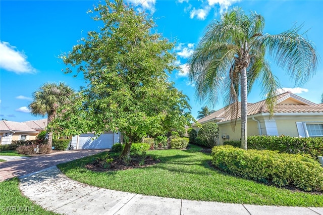 exterior space with a garage, a tiled roof, decorative driveway, a lawn, and stucco siding