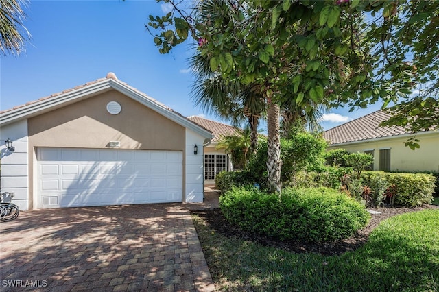 ranch-style home featuring a garage, decorative driveway, a tiled roof, and stucco siding