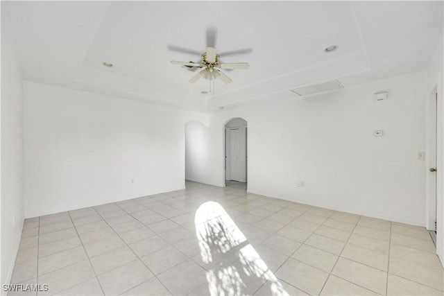 spare room featuring arched walkways, a tray ceiling, light tile patterned floors, and a ceiling fan