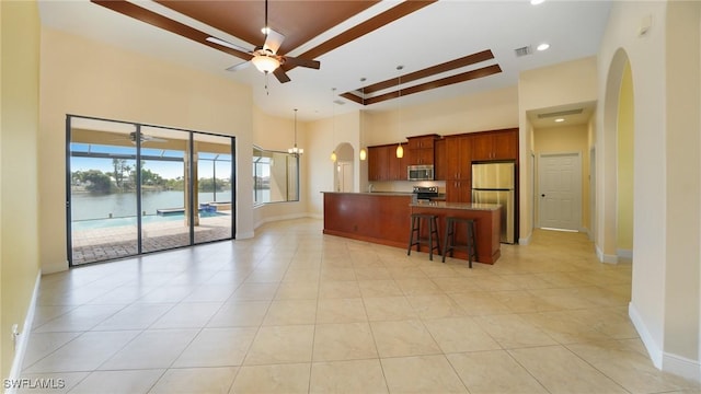 kitchen with a center island, a water view, a high ceiling, appliances with stainless steel finishes, and a kitchen bar