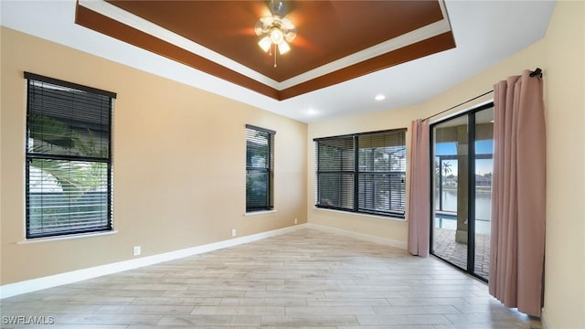 unfurnished room featuring a raised ceiling, a healthy amount of sunlight, ceiling fan, and light hardwood / wood-style floors