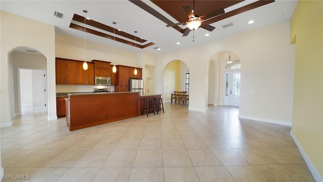 kitchen with a high ceiling, stainless steel appliances, ceiling fan, decorative light fixtures, and a center island