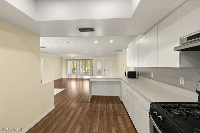 kitchen with kitchen peninsula, gas range, backsplash, white cabinetry, and dark hardwood / wood-style floors