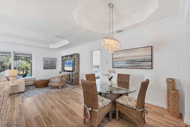 dining room featuring a chandelier, wood finished floors, visible vents, a tray ceiling, and crown molding