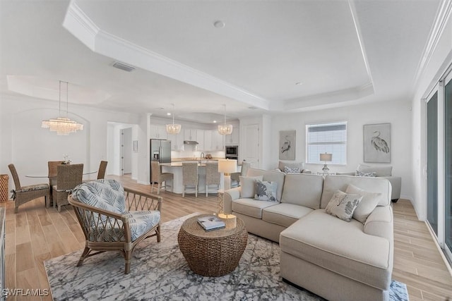 living room featuring light wood-style floors, visible vents, and a raised ceiling