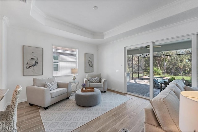 living area featuring wood finish floors, crown molding, a raised ceiling, a sunroom, and baseboards