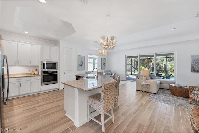 kitchen featuring white cabinets, open floor plan, hanging light fixtures, appliances with stainless steel finishes, and a center island with sink