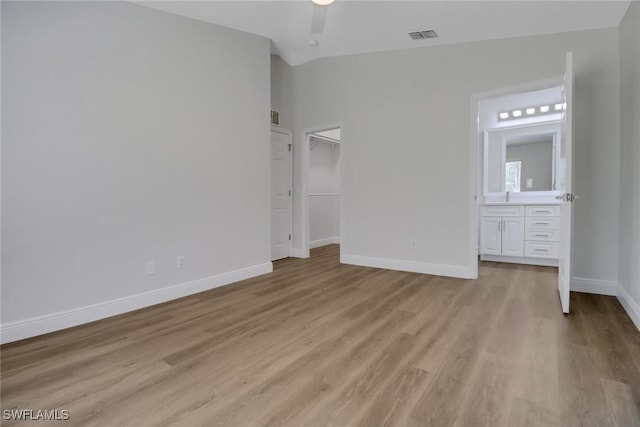 unfurnished bedroom featuring visible vents, baseboards, connected bathroom, light wood-style flooring, and vaulted ceiling