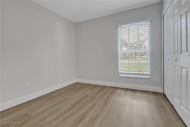 unfurnished bedroom featuring light wood-type flooring, a closet, and baseboards