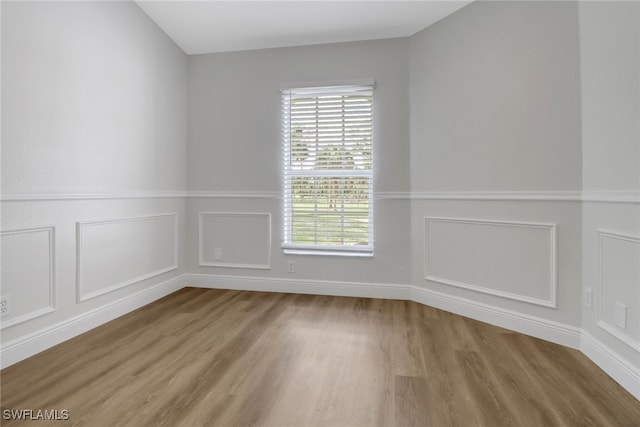 spare room with wainscoting, wood finished floors, and a decorative wall