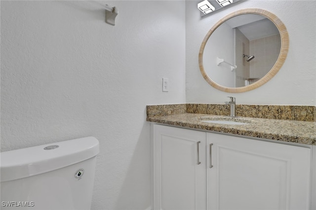 bathroom featuring toilet, a textured wall, and vanity