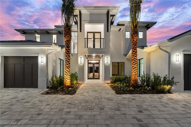 view of front of house featuring a balcony, an attached garage, stucco siding, french doors, and decorative driveway