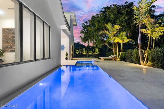 pool at dusk with an outdoor pool and a patio