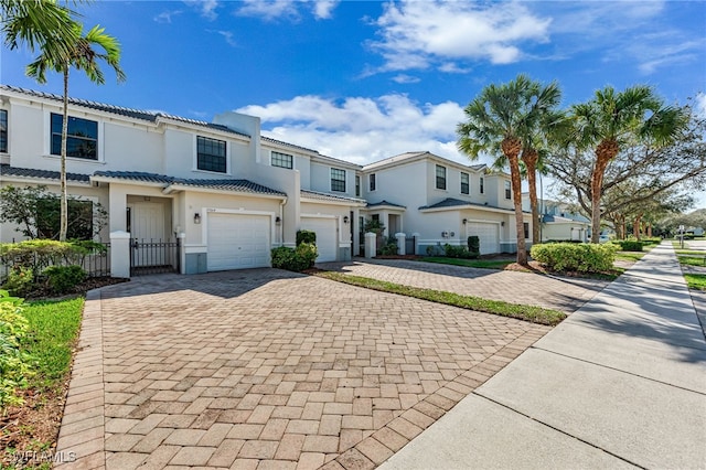 view of property featuring a garage, a tile roof, decorative driveway, and stucco siding