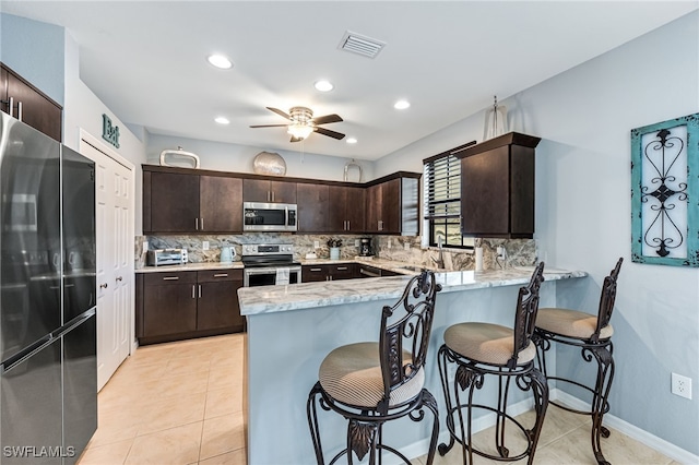 kitchen featuring visible vents, appliances with stainless steel finishes, a sink, dark brown cabinets, and a peninsula