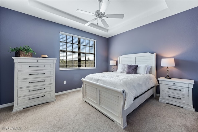 bedroom with light carpet, a tray ceiling, a ceiling fan, and baseboards