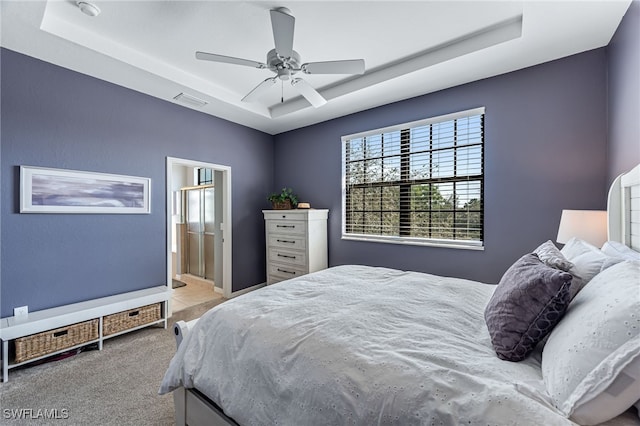 bedroom featuring visible vents, a raised ceiling, connected bathroom, light colored carpet, and ceiling fan