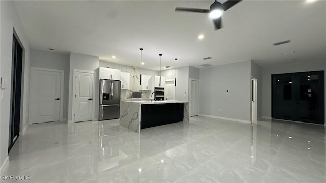 kitchen featuring stainless steel fridge with ice dispenser, an island with sink, marble finish floor, light countertops, and white cabinetry