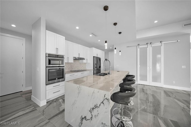 kitchen featuring a center island with sink, white cabinetry, a barn door, hanging light fixtures, and light stone countertops