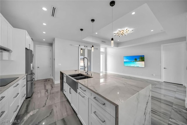 kitchen featuring a center island with sink, a barn door, light stone countertops, white cabinets, and pendant lighting