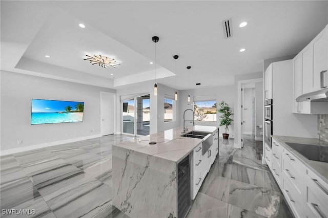 kitchen with light stone countertops, pendant lighting, sink, white cabinetry, and a large island with sink