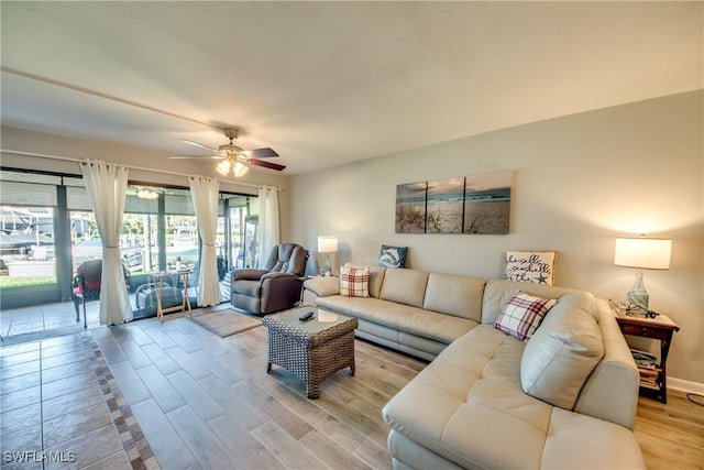 living room with light wood-type flooring, ceiling fan, and baseboards