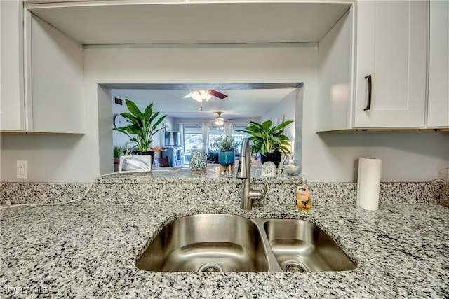 kitchen featuring ceiling fan, a sink, white cabinetry, and light stone countertops